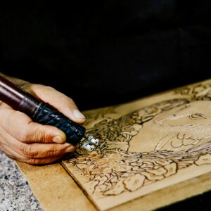 Artisan skillfully engraving intricate designs into leather using precision tool.